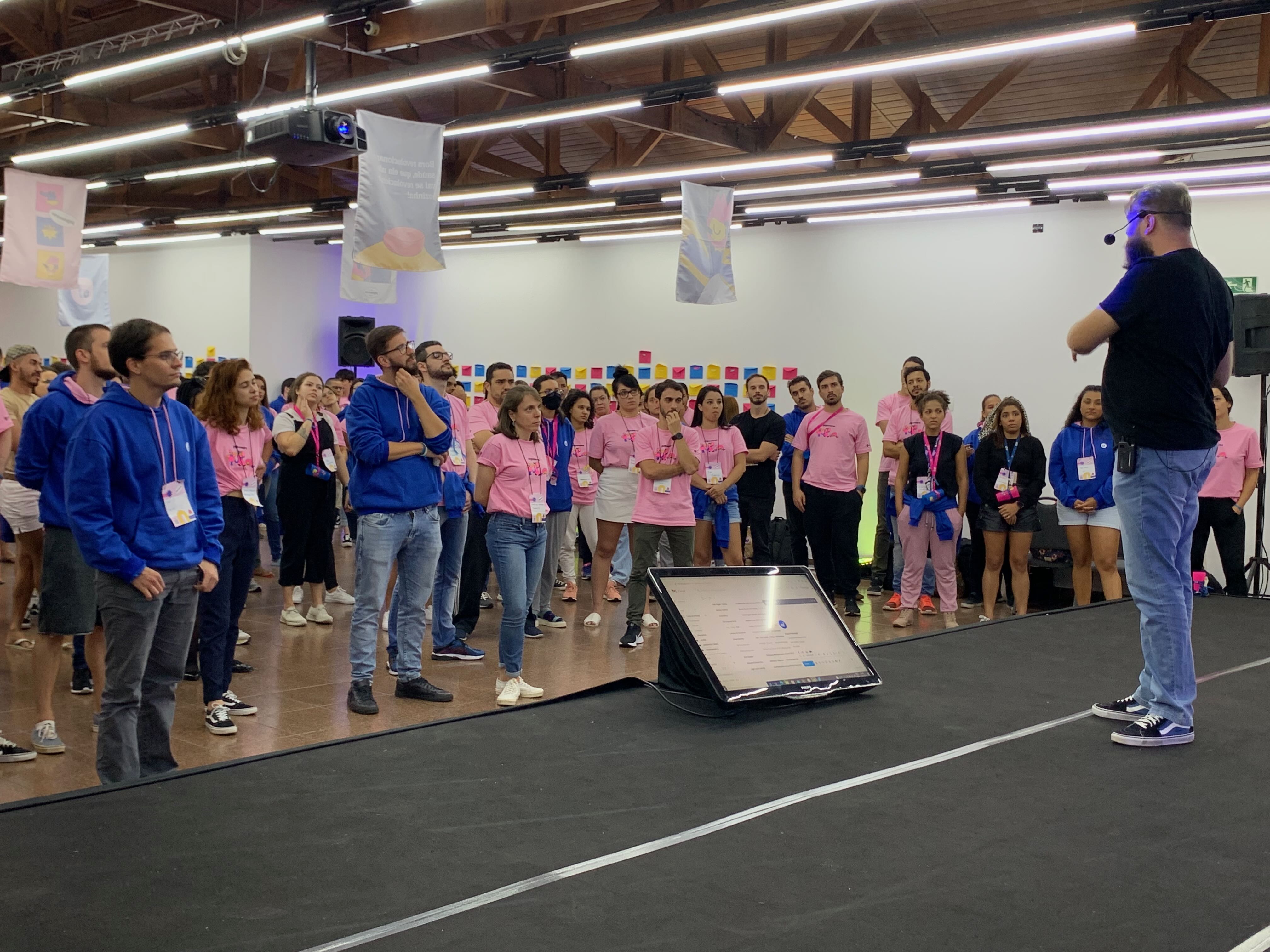 Allan facilitating a group activity with participants in blue and pink t-shirts in a large event hall